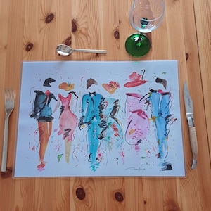 Peut inclure: Un set de table avec une illustration à l'aquarelle de personnages de mode. De la coutellerie, un verre à vin et une cuillère entourent l'œuvre d'art. Le set de table est posé sur une table en bois.