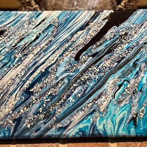 May include: Abstract painting with blue, white, and black paint. The paint has a textured, glittery look.