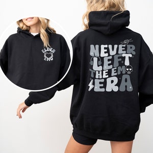 May include: Black hooded sweatshirt with a graphic on the back that says "Never Left The Emo Era" in a retro font with a skull, headphones, and lightning bolt. The front of the sweatshirt has a small graphic that says "Elder Emo" with a heart.
