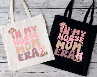 Peut inclure: Deux sacs fourre-tout avec le texte "In My Horse Mom Era" en lettres roses et brunes. Les sacs sont en toile et ont un schéma de couleurs noir et blanc.