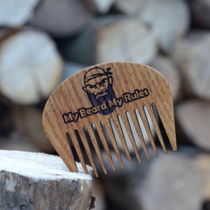 Puede incluir: Un peine de barba de madera con una cara de pirata de dibujos animados y el texto "My Beard My Rules".