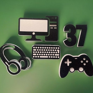 May include: Black and white computer, keyboard, headphones, joystick, and the number 37. These items are cut out of foam and are likely part of a party decoration.