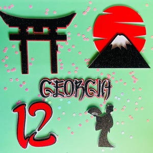 以下が含まれることがあります： 緑色の背景に、日本のテーマの切り抜きが配置されています。黒い鳥居、黒い山のある赤い太陽、「GEORGIA」という名前、「12」の数字、芸者のシルエットが含まれています。ピンク色の紙吹雪が散らばっています。