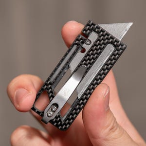 Può includere: Un multiutensile nero e argento con un motivo in fibra di carbonio. Lo strumento ha una lama, un apribottiglie e un cacciavite.