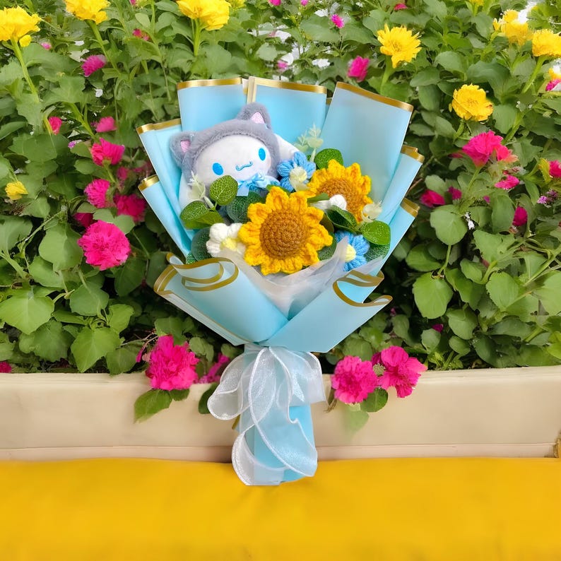 May include: A bouquet featuring a plush character wearing a gray hat, surrounded by crocheted sunflowers and blue flowers. The bouquet is wrapped in light blue paper and tied with a white ribbon, set against a backdrop of colorful flowers.