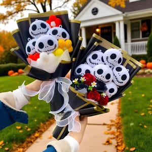 May include: Two bouquets wrapped in black paper with gold trim and white ribbons. Each bouquet features plush white round characters with black stitched eyes and mouths, accented by red and yellow pom-poms or red and black artificial roses.