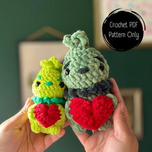 Könnte beinhalten: Zwei gehäkelte Plüschtiere, eines grün und eines grün und schwarz, die rote Herzen halten. Häkel-PDF-Muster nur.