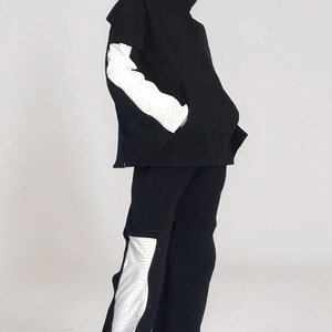 Puede incluir: Un atuendo negro con una chaqueta y pantalones. La chaqueta tiene mangas blancas con lunares y los pantalones tienen un panel blanco con lunares en el lateral. El atuendo se usa con zapatos negros.