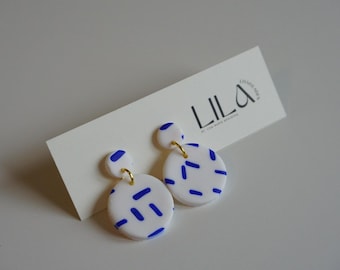 Handmade earrings in white polymer clay with blue stripes and gold-colored details, modern, lightweight and stylish for any occasion.