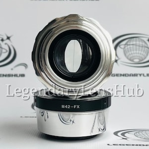 May include: A silver camera lens with a black ring around the middle. The lens has the text "M42-FX" printed on the ring.