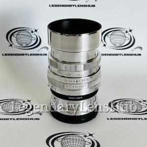 May include: A silver camera lens with a black lens cap. The lens has a silver ring with markings for aperture and distance. The lens is labeled "M42-NEX".