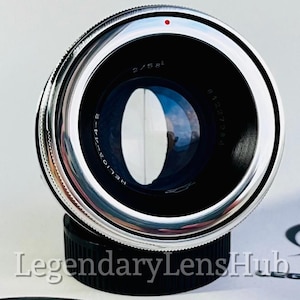 Könnte beinhalten: Ein silbernes und schwarzes Helios-44-2 Objektiv mit einem roten Punkt. Das Objektiv ist auf einem schwarzen Deckel montiert. Der Text "Legendary Lens Hub" ist unten sichtbar.