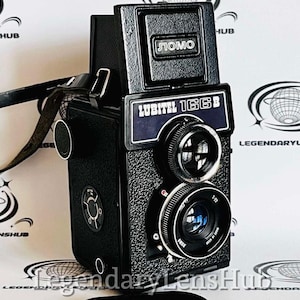 May include: Black Lubitel 166B twin-lens reflex camera with a leather strap. The camera has two lenses, a top viewfinder, and the text "Lubitel 166B" and "LOMO" on the front.