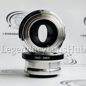 May include: A silver camera lens adapter with a black ring and the text "M42 - M4/3".