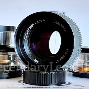 May include: A black camera lens with the text "ЮПИТЕP-37A 3,5/135 837680" printed on the side. The lens is surrounded by several silver and black camera adapters.