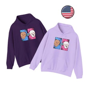 May include: Two hooded sweatshirts with a cartoon graphic of two animals, one brown and one white, with the word "WOW" in a speech bubble. The sweatshirt on the left is purple and the sweatshirt on the right is lavender.