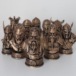 May include: A collection of eight bronze-colored resin busts depicting various warriors and figures with detailed facial features, beards, and helmets, each mounted on a circular base featuring a small circular emblem with a central vertical line.