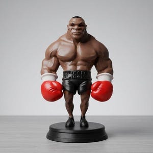 Könnte beinhalten: Eine stilisierte Boxer-Figur mit dunklem Teint und muskulösem Körperbau, bekleidet mit einer schwarzen Hose, auf deren Bund der Schriftzug "MECHA" steht, sowie leuchtend roten Boxhandschuhen mit weißen Bündchen. Die Figur steht auf einem runden schwarzen Sockel.