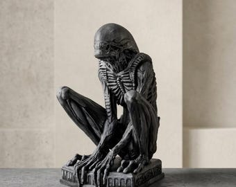 Puede incluir: Una figura de color gris oscuro detallada de una criatura agachada con cabeza alargada, estructuras similares a costillas expuestas y extremidades largas y delgadas. La figura se asienta sobre una base rectangular con arcos.