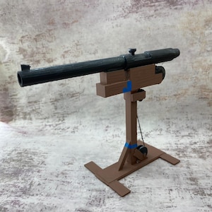 Könnte beinhalten: Eine schwarze Spielzeugkanone, die auf einem braunen Holzständer mit einem Seil- und Flaschenzugsystem montiert ist. Die Kanone ist aus Kunststoff und hat einen Lauf von etwa 30 cm Länge.