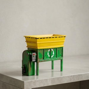 Puede incluir: Una miniatura de máquina de reciclaje verde y amarilla con una tolva rectangular amarilla en la parte superior, una base verde con cuatro patas, un símbolo de reciclaje blanco en el panel frontal y una pequeña caja de control lateral.