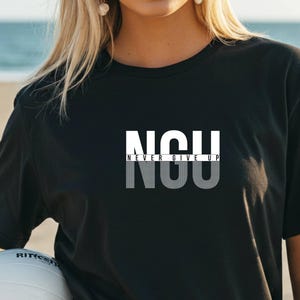 Op de afbeelding: Zwart T-shirt met de tekst "NGU NEVER GIVE UP" in wit en grijs. Het ontwerp is gecentreerd op de borst. Het T-shirt heeft een ronde hals en lijkt gemaakt van zacht materiaal.
