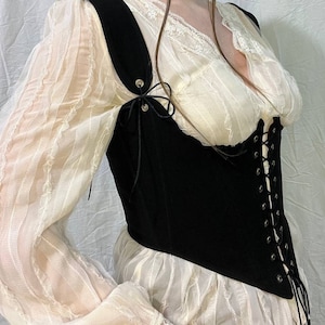 May include: A black corset with a lace-up front and adjustable straps. The corset is worn over a white lace top.