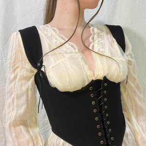 May include: A black corset with a lace-up front and adjustable straps. The corset is made of a thick, sturdy fabric and has a pointed bottom.