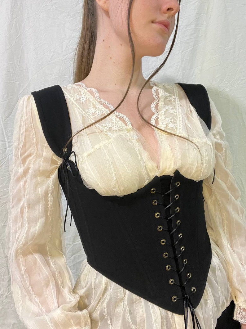 May include: A black corset with a lace-up front and adjustable straps. The corset is made of a thick, sturdy fabric and has a pointed bottom.