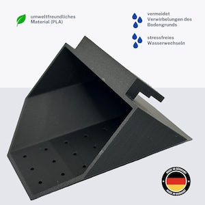 Könnte beinhalten: Schwarzer, 3D-gedruckter Eckenfilter aus Kunststoff für Aquarien mit Löchern für den Wasserfluss. Der Filter besteht aus umweltfreundlichem PLA-Material und hilft, Wasserverwirbelungen zu vermeiden. Der Text "umweltfreundliches Material (PLA)" und "vermeidet Verwirbelungen des Bodengrunds" ist auf dem Bild zu sehen. Der Text "stressfreies Wasserwechseln" ist ebenfalls auf dem Bild zu sehen. Das Bild enthält auch ein "Made in Germany"-Logo mit der deutschen Flagge.