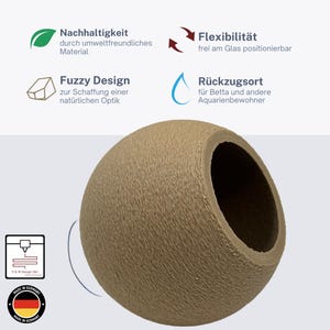 May include: A tan, spherical aquarium hideaway with a textured surface. The product has a large opening and is designed for aquatic pets. Text on the image includes "Fuzzy Design" and "Made in Germany."