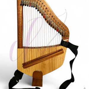 Puede incluir: Un arpa de lira de madera con un cuerpo de madera clara y un mástil de madera más oscura. El arpa tiene cuerdas y clavijas de afinación con acentos coloridos. Se adjunta una correa negra para llevarla. El logotipo de Ukona Harps está en la esquina inferior derecha.