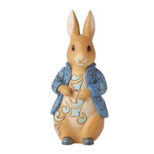 Può includere: Statuetta di coniglio in piedi, con pelliccia marrone chiaro, indossa una giacca blu con un motivo floreale. Il coniglio ha lunghe orecchie e mani giunte. Sfondo bianco.