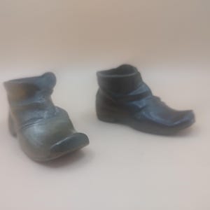 May include: Two small, black leather boots with a pointed toe. The boots are made of a textured material and have a simple design.