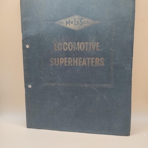 Puede incluir: Un libro azul oscuro con el título "LOCOMOTIVE SUPERHEATERS" en letras doradas. El libro tiene un logotipo dorado en forma de diamante con el texto "MELESCO" en su interior.