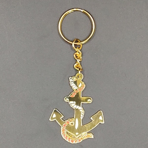 Op de afbeelding: Goudkleurige anker sleutelhanger met rode en witte touwdetails. Het anker is bevestigd aan een goudkleurige ketting en een goudkleurige sleutelring. Een nautisch thema accessoire.
