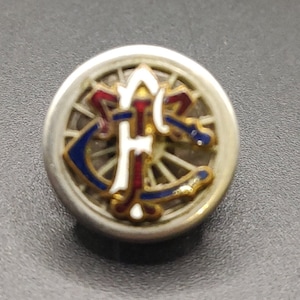 May include: A silver-toned button with a blue, red and white enamel design. The design features a stylised anchor and a wheel with spokes.