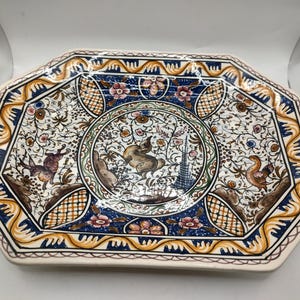 May include: Octagonal ceramic serving platter with a white background and a colourful floral design. The centre features a circular design with a green border and a white background with a floral pattern and a brown rabbit. The border of the platter is decorated with a yellow, blue and orange pattern.