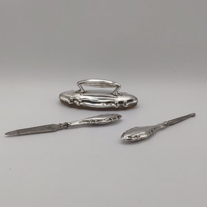 Könnte beinhalten: Ein silbernes Maniküre-Set mit einer Nagelfeile, einem Nagelhaut-Schieber und einem kleinen, ovalen Etui.