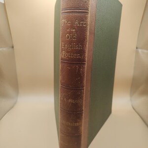May include: A brown leather-bound book with gold lettering on the spine. The title is "The Art of the Old English Potter".