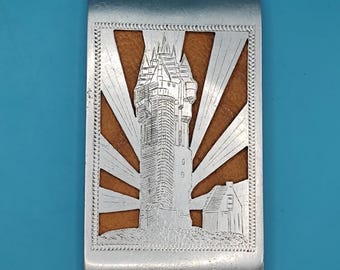 May include: Silver money clip featuring a castle tower engraving and sunburst design. The interior has a brown leather insert. The rectangular clip has a decorative edge. A practical and stylish accessory.