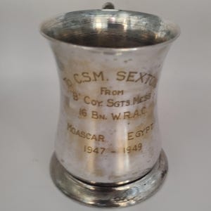 Puede incluir: Una copa de plata con una inscripción que dice "To CSM. Sexton From B' Coy. Sgts. Mess 16 Bn. W.R.A.C. Moascar Egypt 1947 - 1949".
