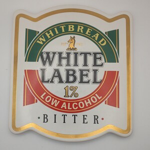 May include: A white, gold, green, and red beer coaster with the text "Whitbread White Label 1% Low Alcohol Bitter" on it.