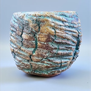 May include: A handcrafted ceramic bowl with a textured, bark-like exterior. The bowl features a blend of brown, turquoise, and white hues, with visible cracks and a rough surface. The unique design gives it a rustic, organic aesthetic, suitable for home decor.