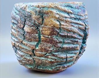May include: A handcrafted ceramic bowl with a textured, bark-like exterior. The bowl features a blend of brown, turquoise, and white hues, with visible cracks and a rough surface. The unique design gives it a rustic, organic aesthetic, suitable for home decor.