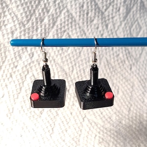 May include: A pair of black and red joystick earrings. The earrings are shaped like a classic video game joystick with a red button.