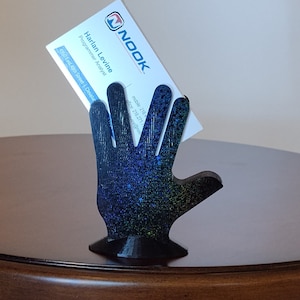 May include: A black 3D printed hand shaped like the Vulcan salute holds a business card with the text "NOOK" and "Harlan Levine, Programmer Analyst" printed on it.