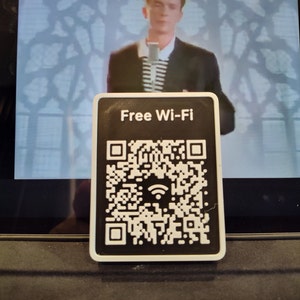 May include: A white plastic sign with black text that reads "Free Wi-Fi" and a black and white QR code with a wifi symbol in the center.