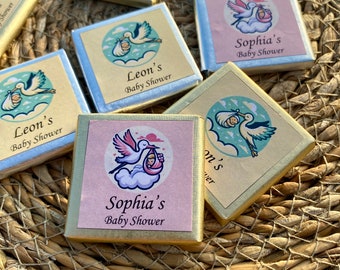 May include: A collection of small, square, gold, silver, and pink boxes with baby shower favors. Each box features a stork carrying a baby and the text "Sophia's Baby Shower" or "Leon's Baby Shower".