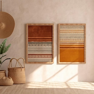 Op de afbeelding: Twee ingelijste abstracte kunstprints met geometrische patronen in bruin- en oranjetinten hangen aan een neutrale muur. Een geweven hoed, een potplant en geweven manden dragen bij aan de bohemien inrichting. De kamer baadt in natuurlijk licht.